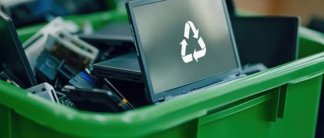 A pile of laptops in a green recycling bin, with a clear recycling logo in focus, highlighting the importance of e-waste recycling